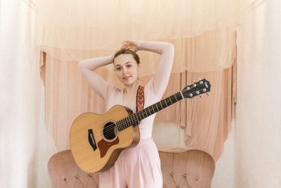 一个穿着粉色无袖连衣裙拿着棕色原声吉他的女人